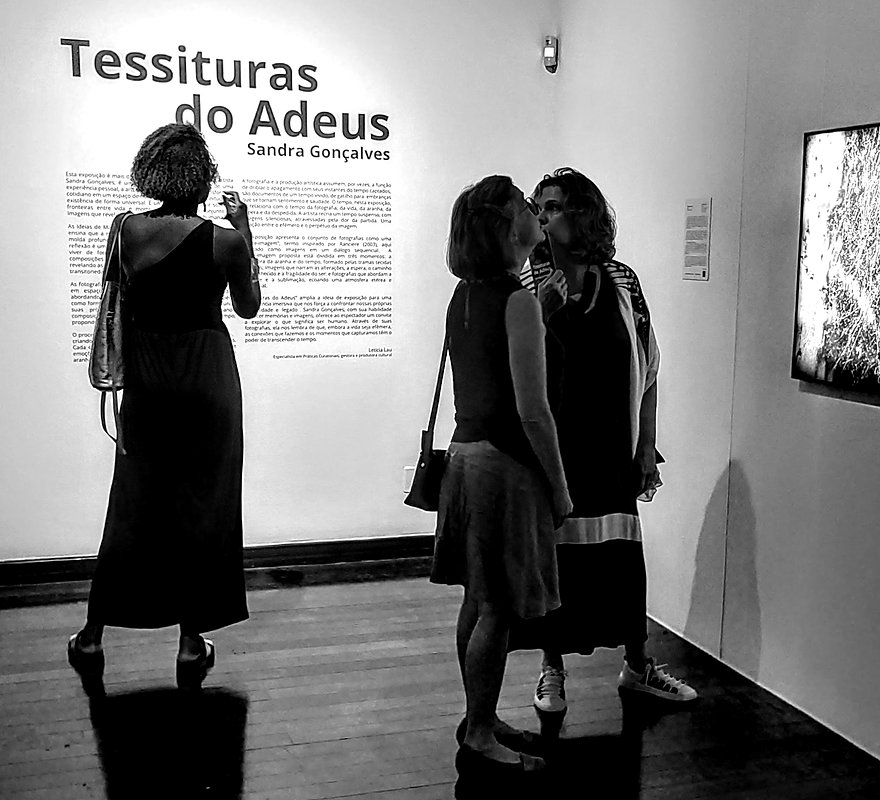 Visitantes diante do texto curatorial da exposição Tessituras do Adeus